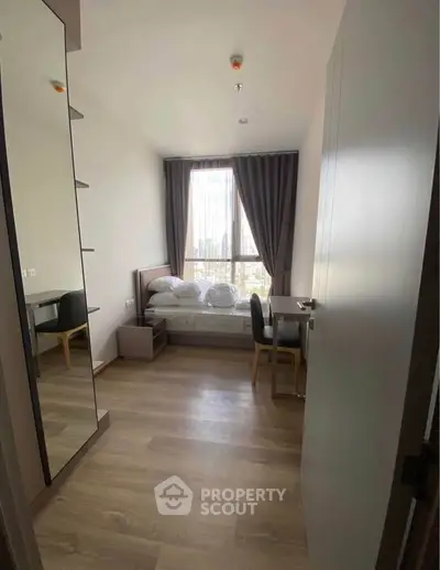 Cozy bedroom with modern furnishings and large window offering city views, perfect for urban living.
