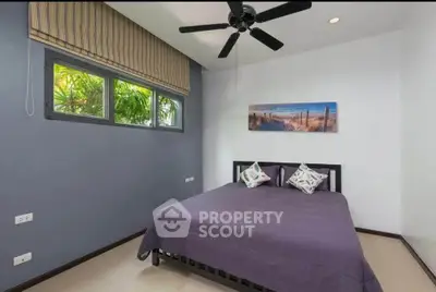 Modern bedroom with ceiling fan and large window, featuring stylish decor and natural light.