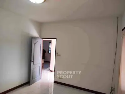 Spacious empty room with white walls and tiled floor, featuring a single door and natural light.