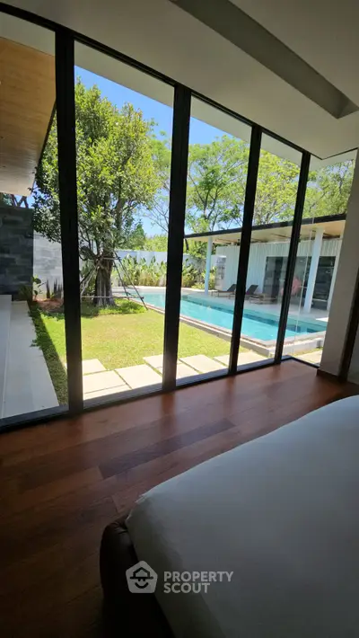 Luxurious bedroom with floor-to-ceiling windows overlooking a serene pool and lush garden.