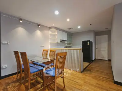 Spacious dining area with wooden flooring and modern kitchen in open layout apartment.