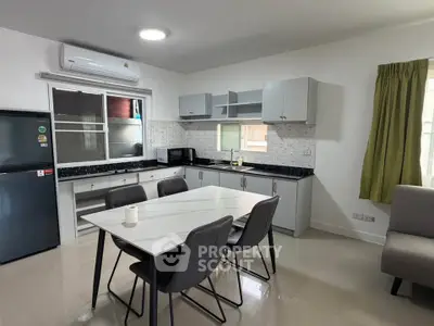 Modern kitchen with sleek design, featuring a dining table and chairs, air conditioning, and ample cabinetry.