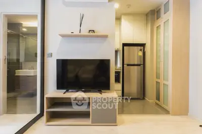 Modern living room with sleek TV setup and compact kitchen area in stylish apartment.