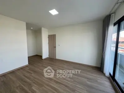 Spacious empty living room with wooden flooring and large window for natural light.