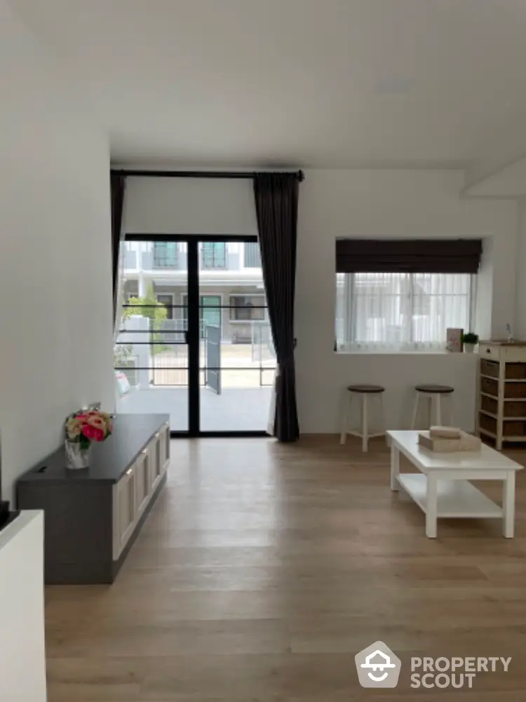 Spacious and modern living room with sleek hardwood floors, abundant natural light, and a cozy minimalist design, leading to a charming balcony.