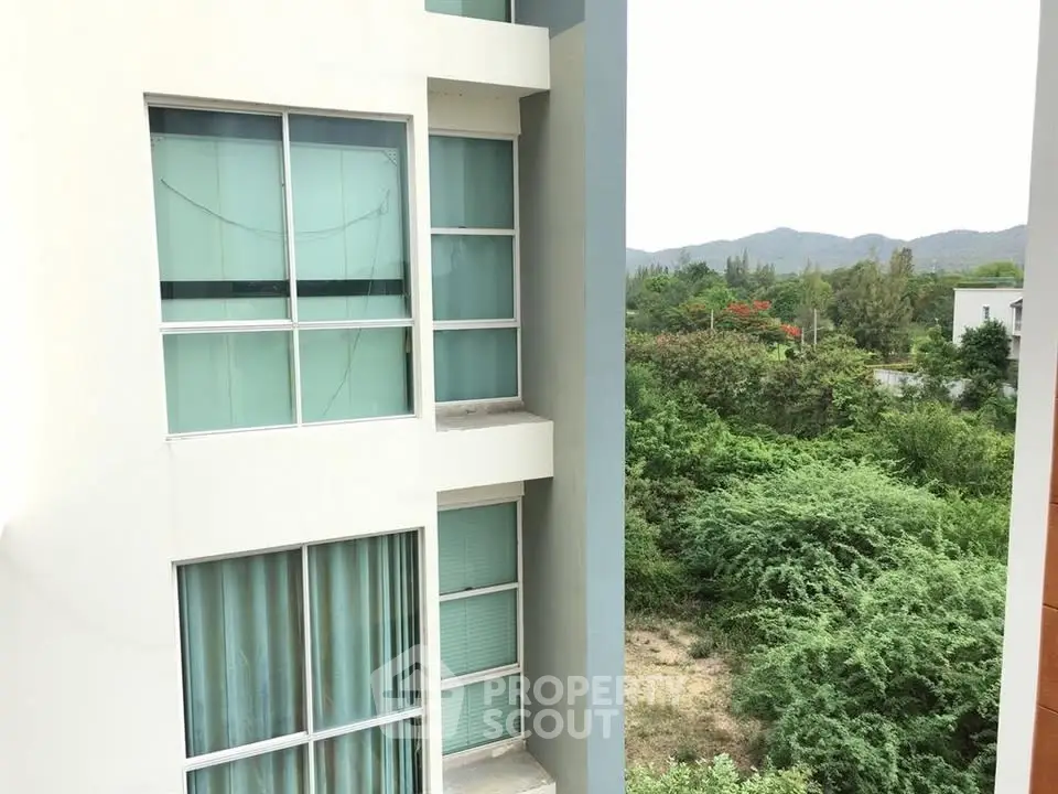 Modern apartment building exterior with lush green surroundings and mountain view.