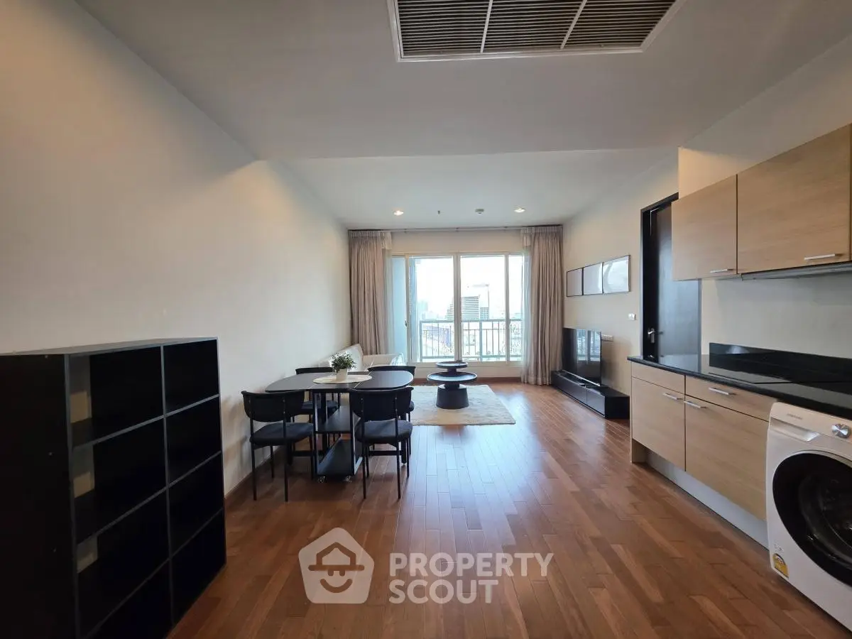Spacious modern living room with wooden flooring and open layout, featuring a dining area and balcony access.
