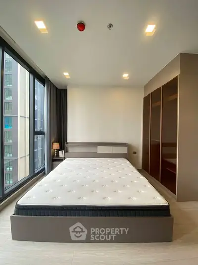 Modern bedroom with large window and built-in wardrobe in high-rise apartment