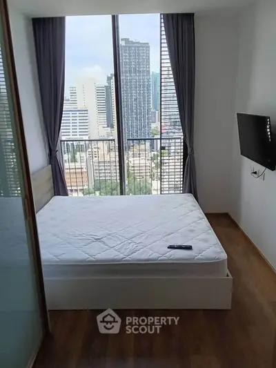 Modern bedroom with city view, floor-to-ceiling windows, and wall-mounted TV in a high-rise apartment.