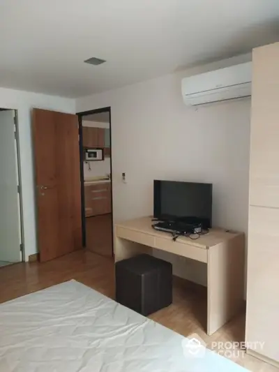 Modern bedroom with TV and air conditioning, featuring wooden flooring and neutral decor.