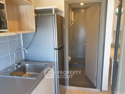 Modern compact kitchen with stainless steel sink and fridge, leading to a bathroom.