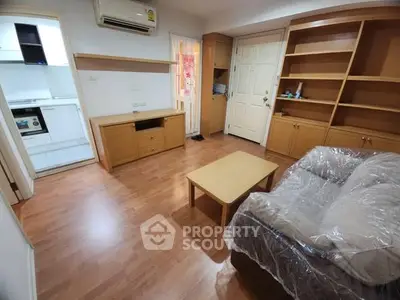 Cozy living room with wooden flooring and built-in shelves, adjacent to a compact kitchen.