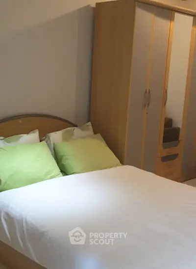 Cozy bedroom with wooden wardrobe and double bed featuring green pillows.