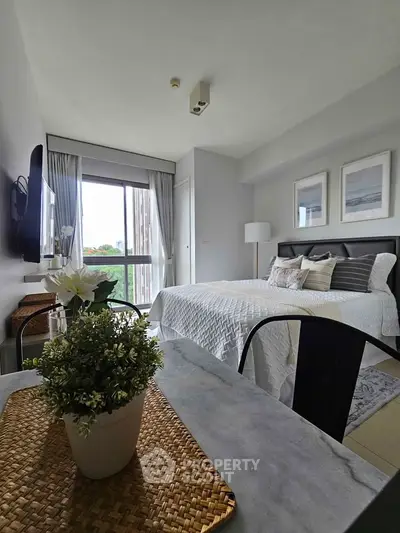 Modern bedroom with stylish decor and large window offering natural light and greenery view.