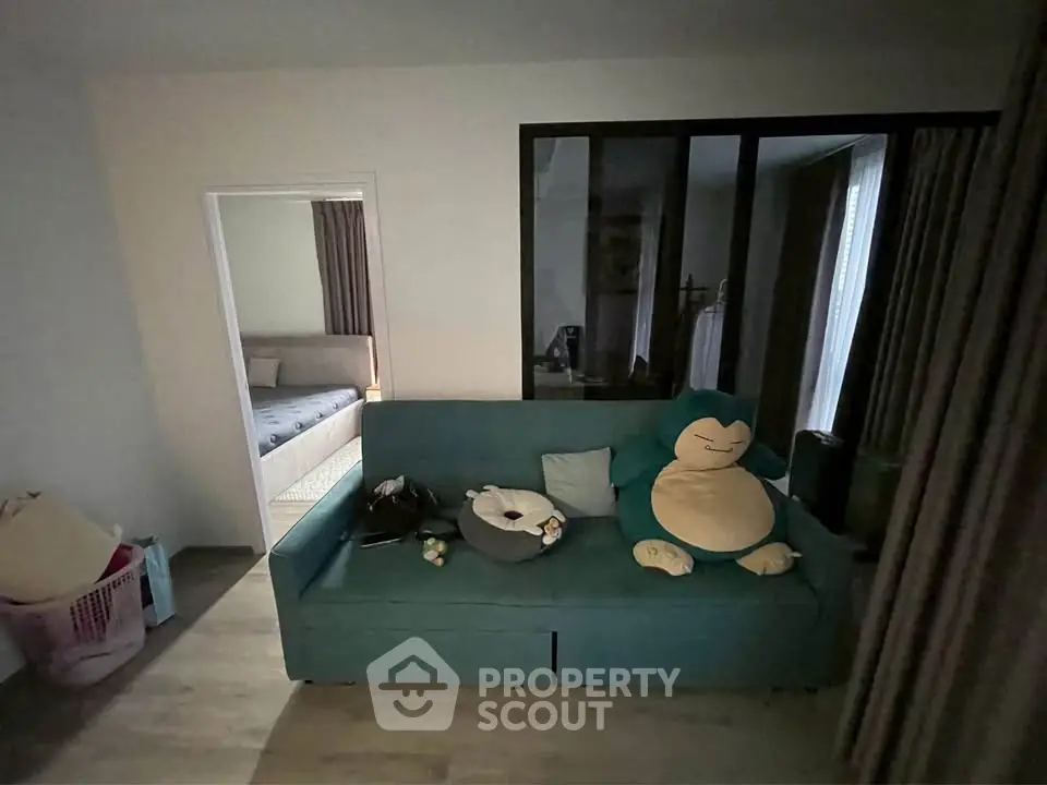 Cozy living room with teal sofa and plush toys, adjacent to a bedroom with soft lighting.