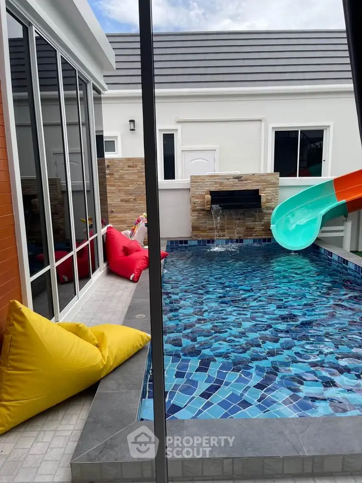 Charming private pool with colorful slide and cozy seating in modern home exterior.