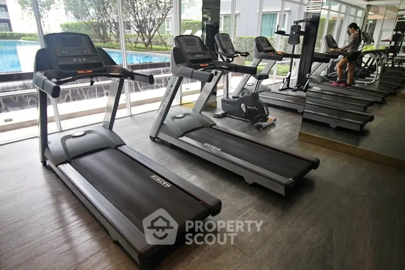 Modern gym with treadmills and pool view in luxury apartment complex.