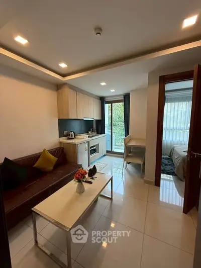 Modern living room with open kitchen and balcony view, featuring sleek furniture and natural light.