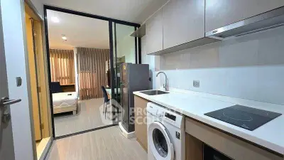 Modern apartment kitchen with washing machine and open layout to living area.