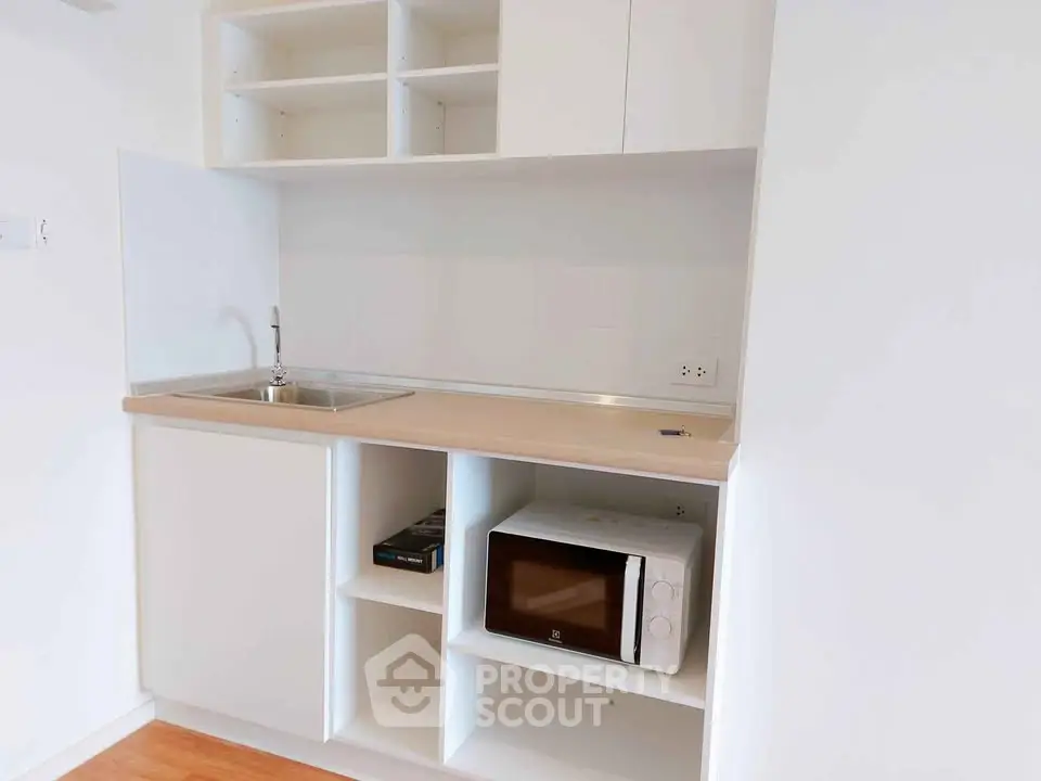 Modern compact kitchen with microwave and sleek cabinetry in a minimalist apartment.