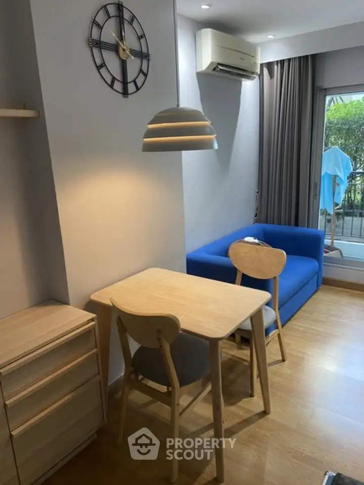 Cozy living room with modern furniture and natural light, featuring a blue sofa and wooden dining set.