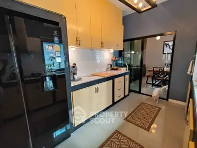 Modern kitchen with sleek black fridge and yellow cabinets, open layout to dining area.