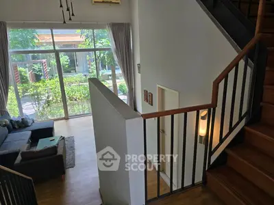 Spacious living room with large windows and wooden staircase, offering a bright and airy ambiance.
