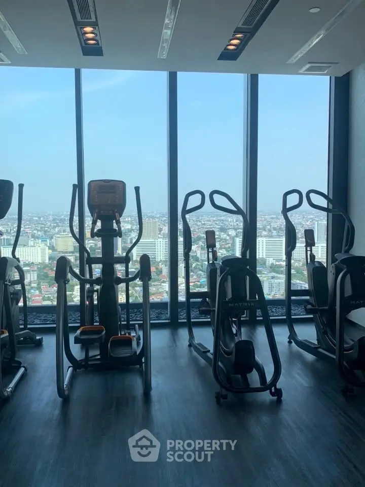 Modern gym with city view through large windows, featuring exercise equipment.
