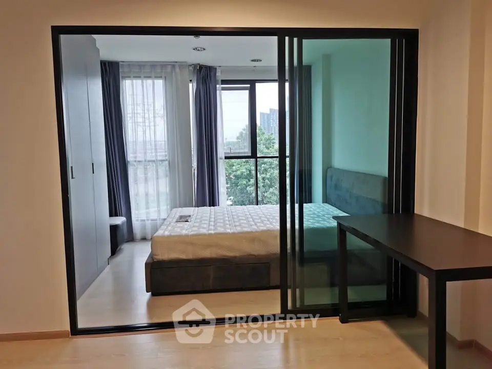 Modern bedroom with sliding glass doors and natural light, featuring a cozy bed and sleek furnishings.