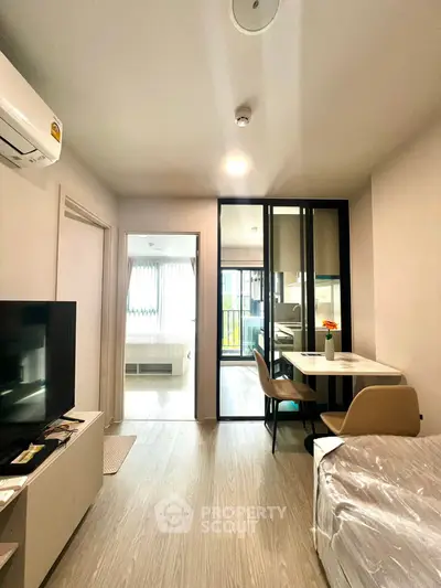 Modern living room with dining area and view into bedroom, featuring sleek design and natural light.