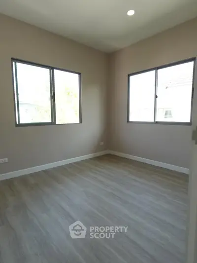 Spacious empty bedroom with large windows and wooden flooring, perfect for customization.