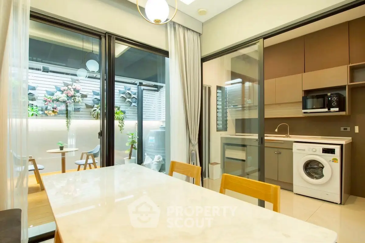 Modern kitchen with washing machine and dining area, featuring sleek design and outdoor view.