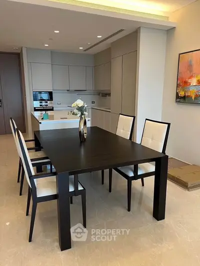 Modern dining area with sleek black table and chairs, adjacent to a contemporary kitchen with built-in appliances.