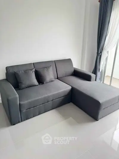 Modern gray sofa in a bright living room with large windows and elegant curtains.