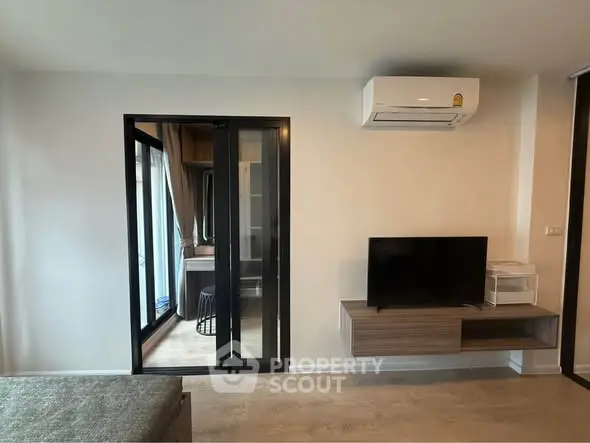 Modern living room with sleek TV setup and air conditioning, featuring a glass door to a cozy balcony.