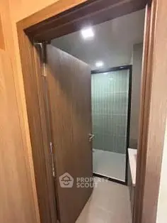 Modern bathroom entrance with wooden door and tiled shower area.
