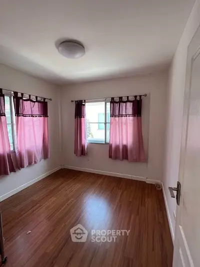 Spacious bedroom with wooden flooring and pink curtains, perfect for cozy living.