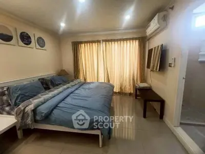 Cozy bedroom with large bed, wall-mounted TV, and natural light from curtains.