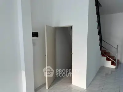 Modern interior with staircase and storage space under stairs, featuring sleek white walls and tiled flooring.