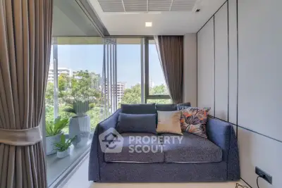 Modern living room with large windows and lush greenery view, featuring a cozy sofa and elegant curtains.