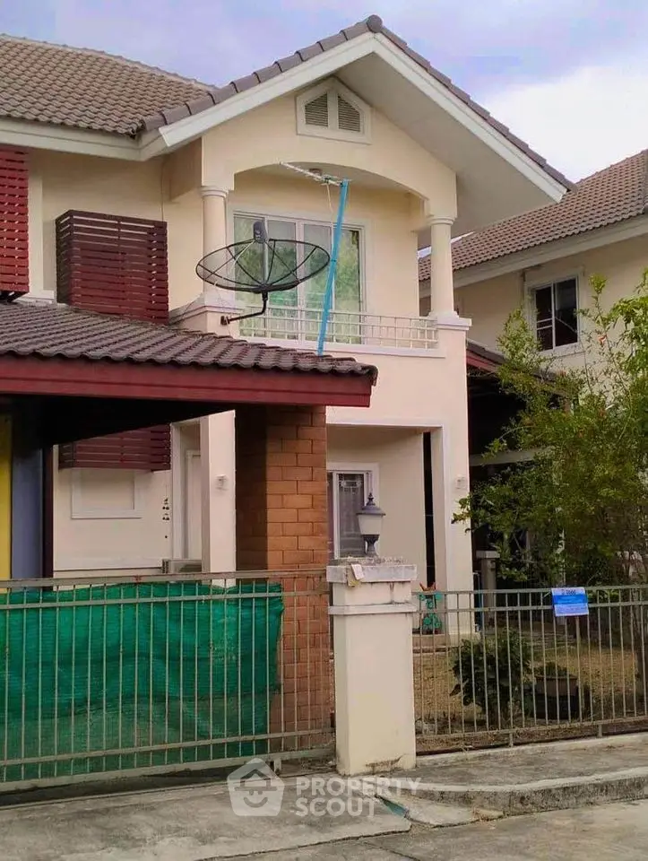 Charming two-story family home with a spacious balcony and red tile roofing, nestled in a serene neighborhood with lush greenery.
