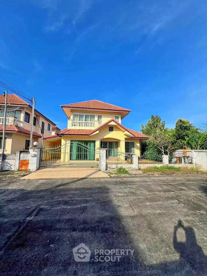 Charming two-story yellow house with red roof and gated entrance in a serene neighborhood.