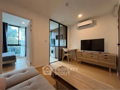 Modern living room with open layout, featuring a cozy sofa, TV, and a view into the bedroom and kitchen.