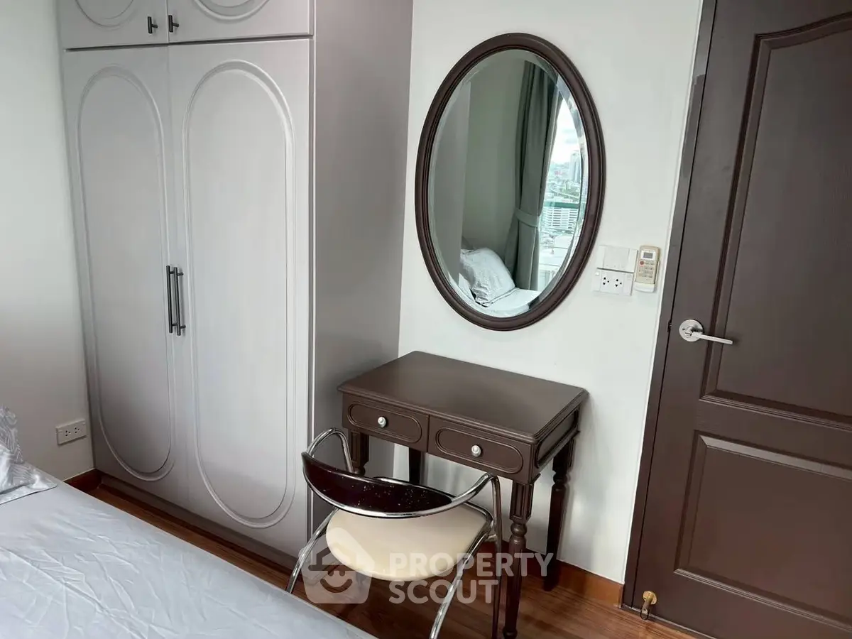Cozy bedroom with elegant vanity and wardrobe, featuring a stylish chair and oval mirror.