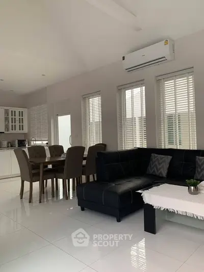 Modern open-plan living room with sleek black sofa and dining area, featuring large windows and air conditioning.