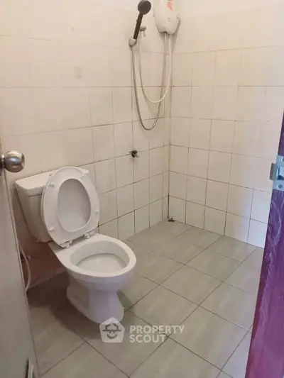 Simple bathroom with tiled walls and floor, featuring a toilet and showerhead.