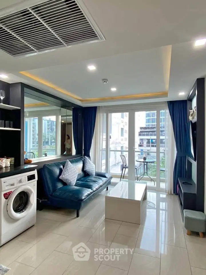 Modern living room with blue sofa, washing machine, and balcony view in urban apartment.
