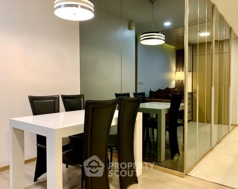 Modern dining area with sleek white table, black chairs, and mirrored wall for spacious feel.
