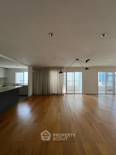 Spacious modern living room with wooden floors and large windows in urban apartment.