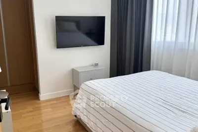 Modern bedroom with wall-mounted TV and striped bedding in a bright apartment.